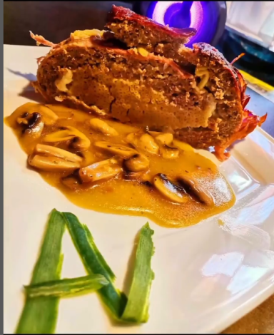 Ein Stück Fleisch mit einer Beilage aus Nüssen und einer Sauce auf einem Teller.