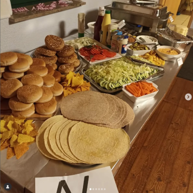 Ein Tisch mit Hamburger-Brötchen, frischem Gemüse und verschiedenen Beilagen.